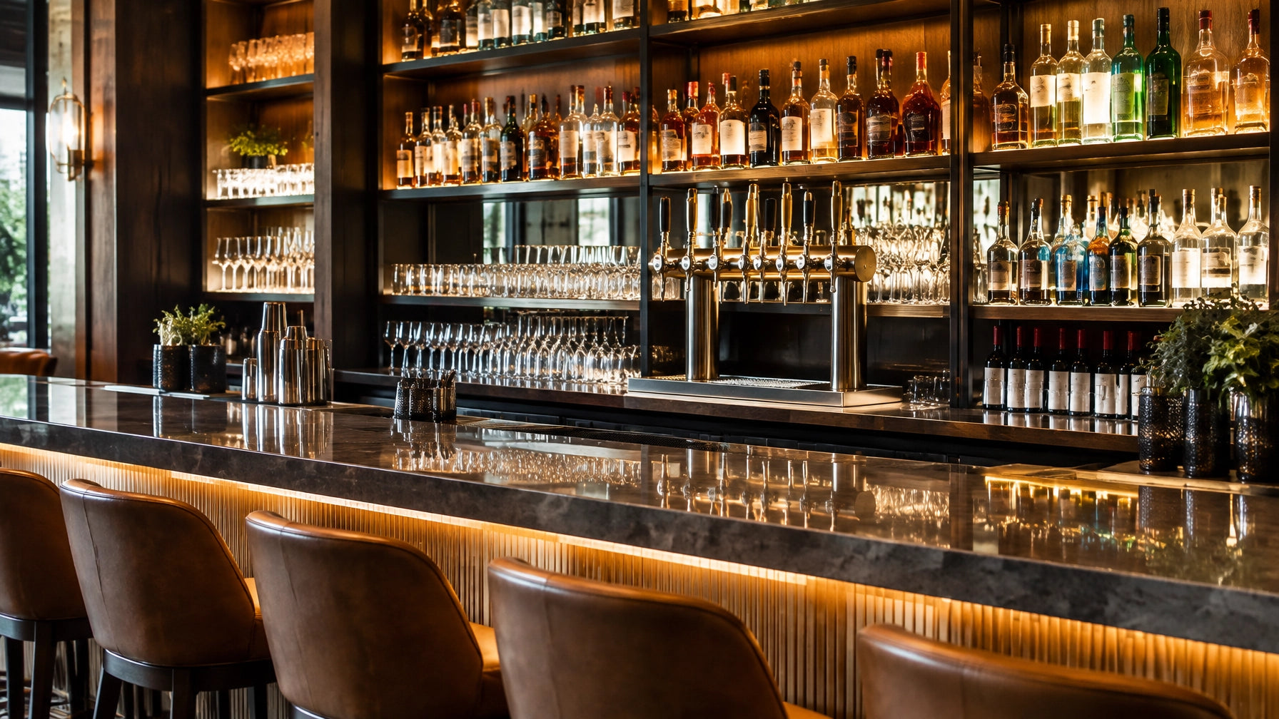 Modern bar interior with warm lighting, a polished counter, draft taps, back-bar bottles and glassware.