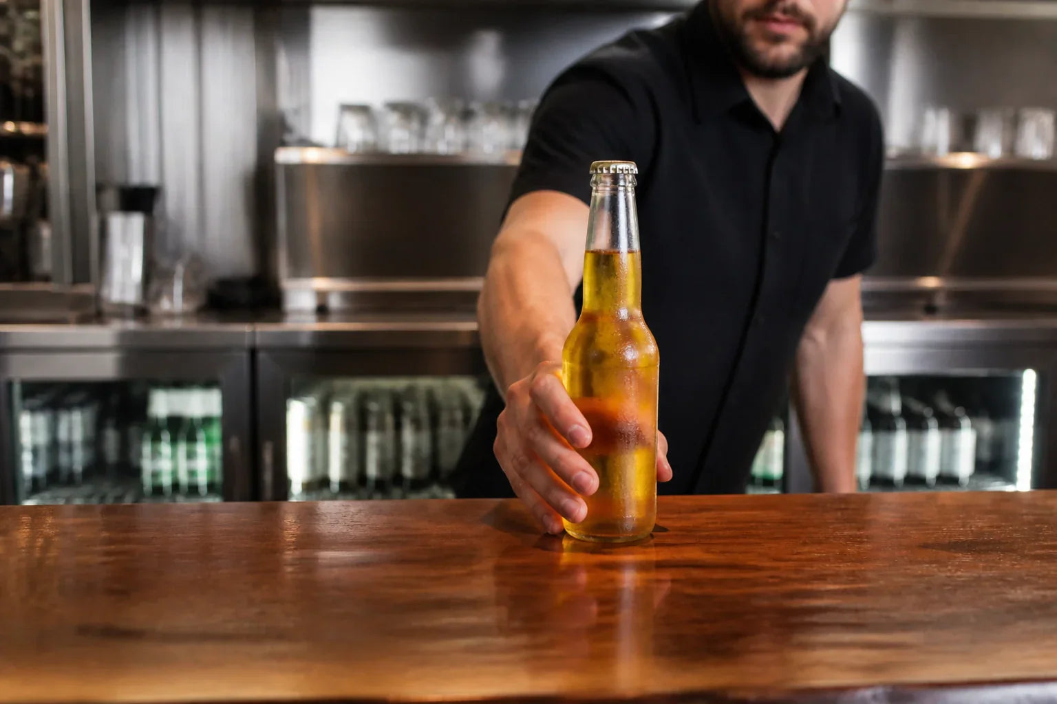 A professional bartender placing a cold beer on a counter in a high-end commercial bar.