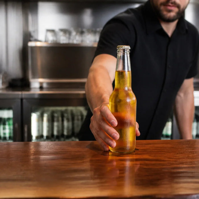 A professional bartender placing a cold beer on a counter in a high-end commercial bar.
