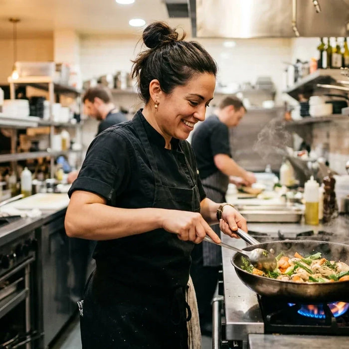 A professional chef cooking at a commercial restaurant range in a clean, welcoming kitchen with warm lighting, stainless steel equipment, and an inviting professional atmosphere