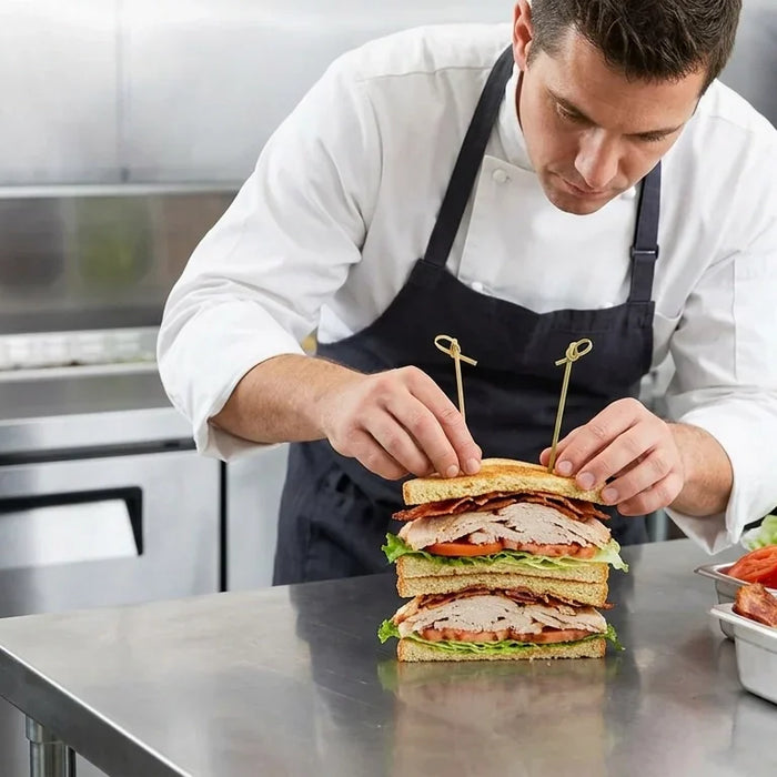 A professional chef assembling a turkey club sandwich on a stainless steel worktable