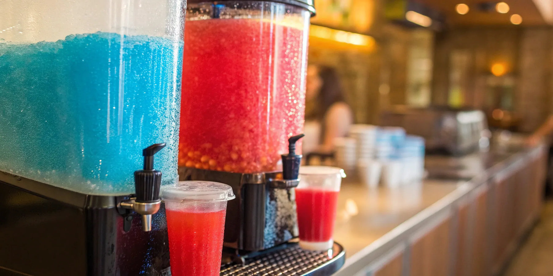 Red and blue slushie machines dispense frozen drinks.