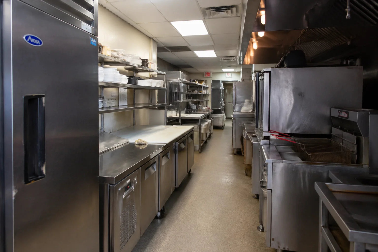 Industrial commercial kitchen prep line featuring stainless steel worktables and Atosa equipment in a narrow corridor