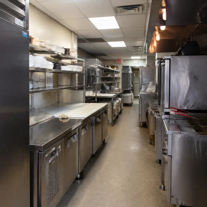 Industrial commercial kitchen prep line featuring stainless steel worktables and Atosa equipment in a narrow corridor