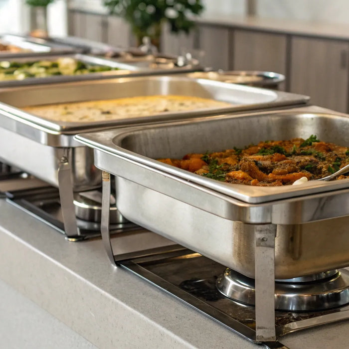 Various sizes of stainless steel catering pans holding hot food on a buffet.