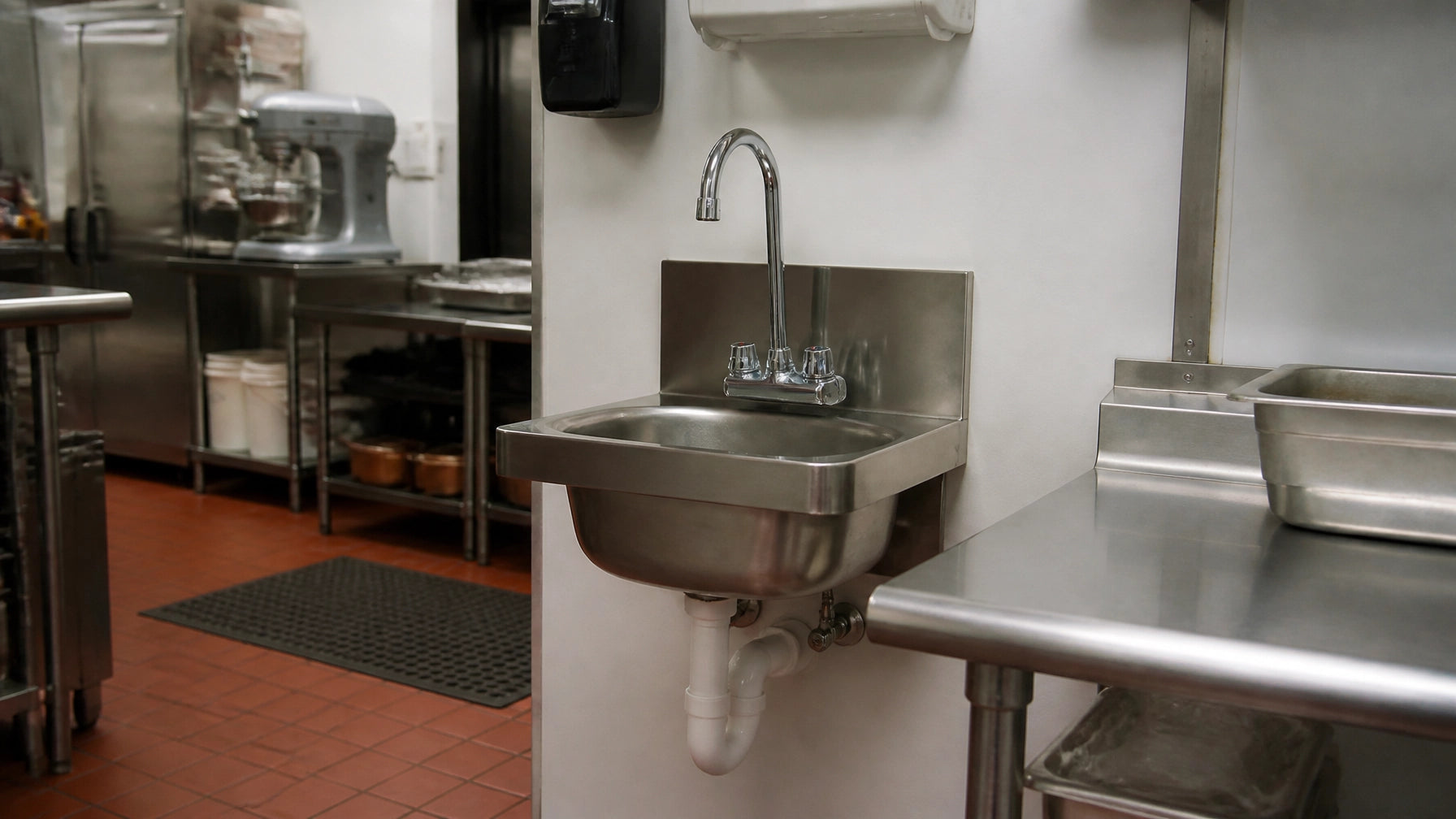 Stainless steel commercial hand sink wall-mounted in a restaurant kitchen with gooseneck faucet, soap dispenser, paper towel dispenser, and side splash guards