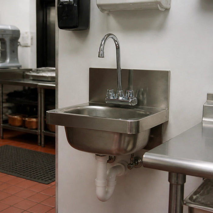 Stainless steel commercial hand sink wall-mounted in a restaurant kitchen with gooseneck faucet, soap dispenser, paper towel dispenser, and side splash guards