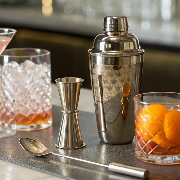 Bartender supply store counter with a cocktail shaker, jigger, bar spoon, and glassware.