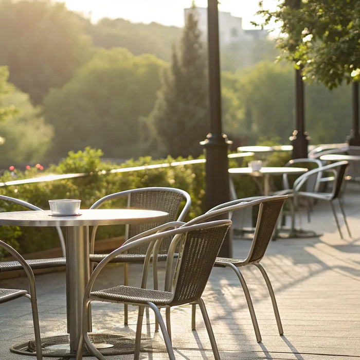 Outdoor restaurant chairs and tables on a sunny patio surrounded by greenery.