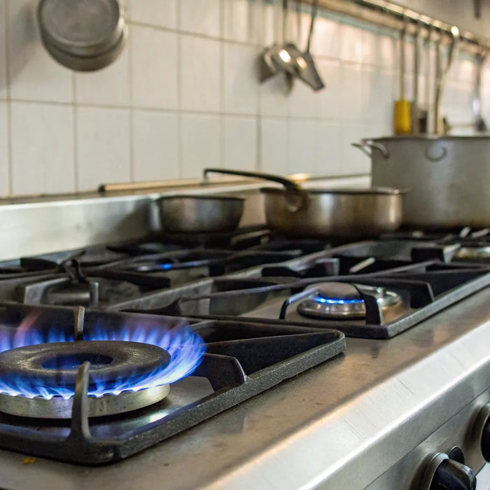 Restaurant propane stove with pots and blue flames.