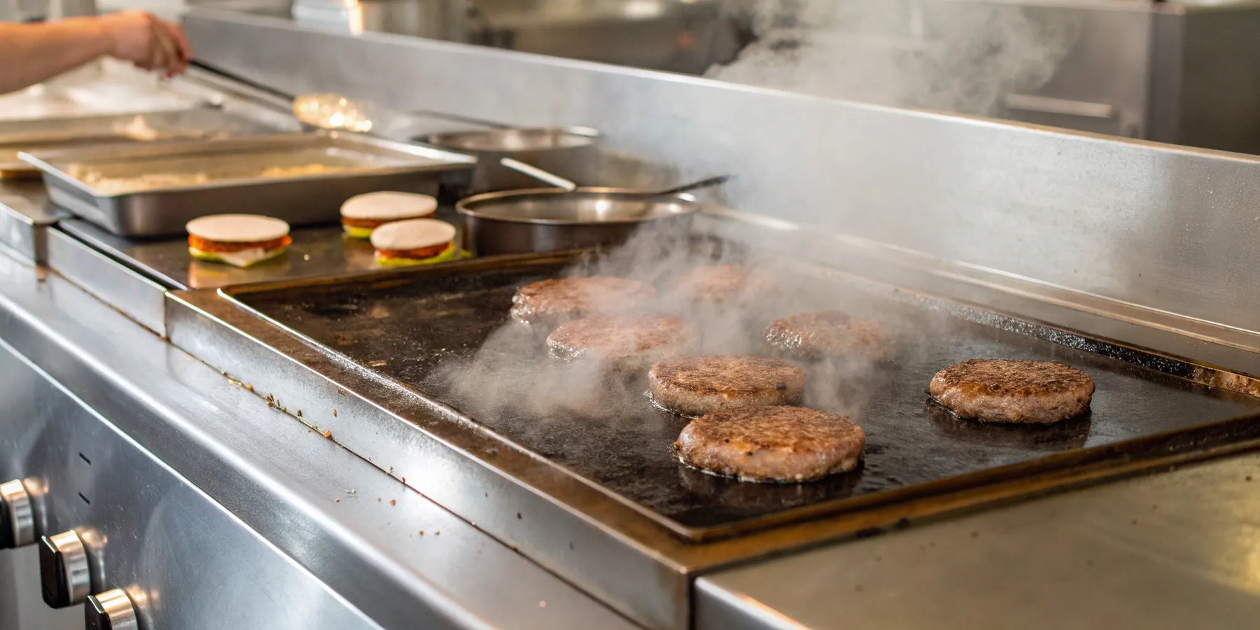 Burger patties sizzling on a hot restaurant griddle as steam rises.