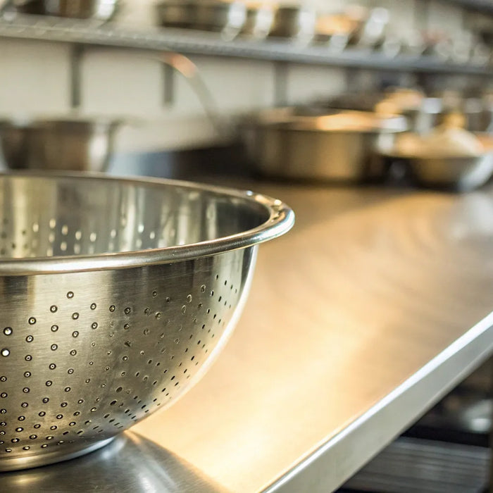 A professional stainless steel collandee on a commercial kitchen counter, ready for fast drainage.