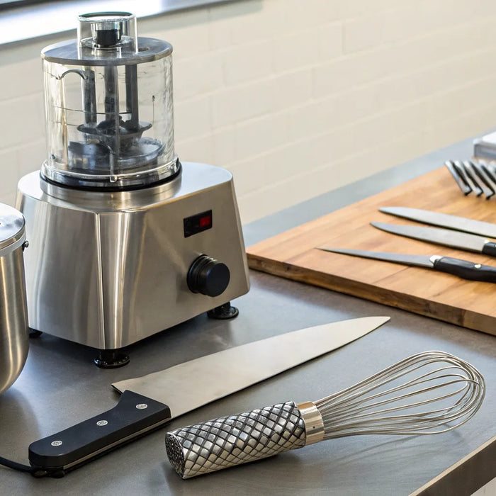 Essential restaurant accessories including knives, a pot, and a whisk on a stainless steel prep counter.