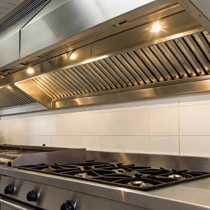 Commercial kitchen hood system over stainless steel appliances.